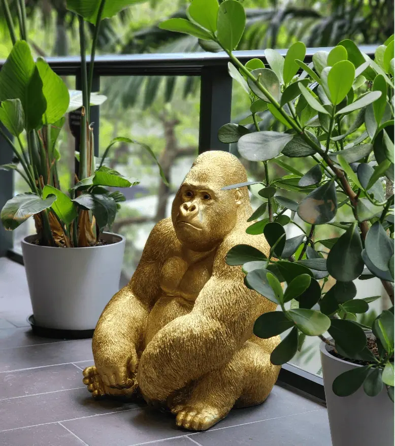 A golden gorilla statue sits among green potted plants on a balcony with a glass railing, creating an oasis that small businesses can replicate for their own unique charm.