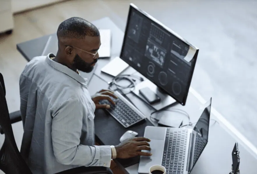 A person working at a desk with two computers, focusing on screens displaying data and charts essential for small businesses.