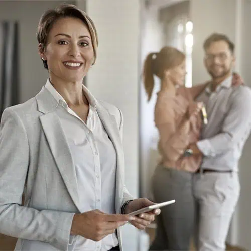 A person in a suit smiles at the camera while holding a tablet, perhaps discussing Project Finance. In the background, a couple embraces and smiles, one holding a drink.