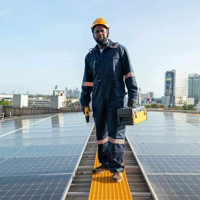 A technician wearing a hard hat and uniform stands on a rooftop with solar panels, holding a toolbox and a drill, seamlessly merging technical expertise with project finance management, city buildings standing tall in the background.