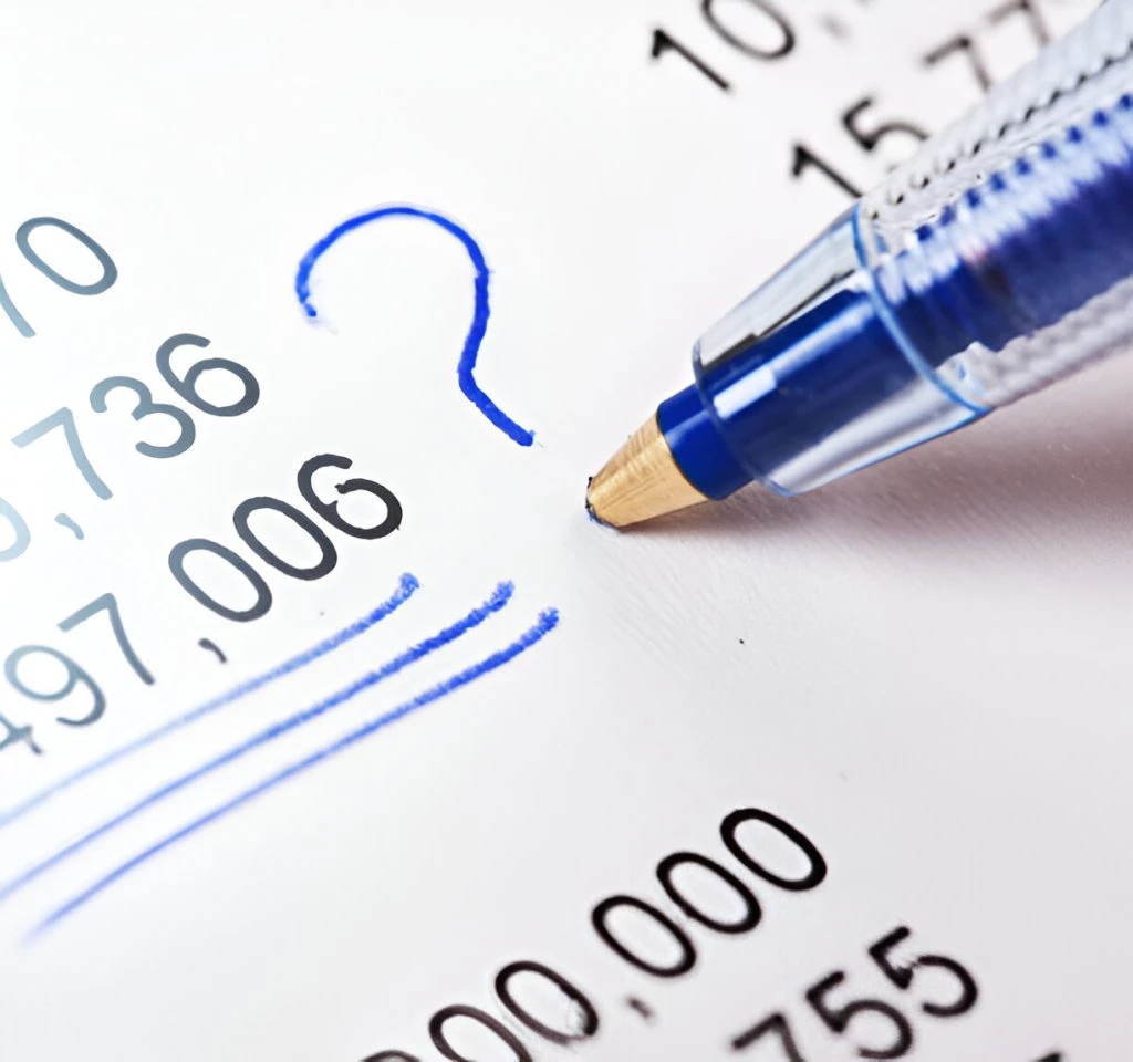 Close-up of a blue pen pointing at a list of numbers on paper, with a blue question mark drawn beside one figure, highlighting uncertainty and potential bookkeeping mistakes small business owners might face.