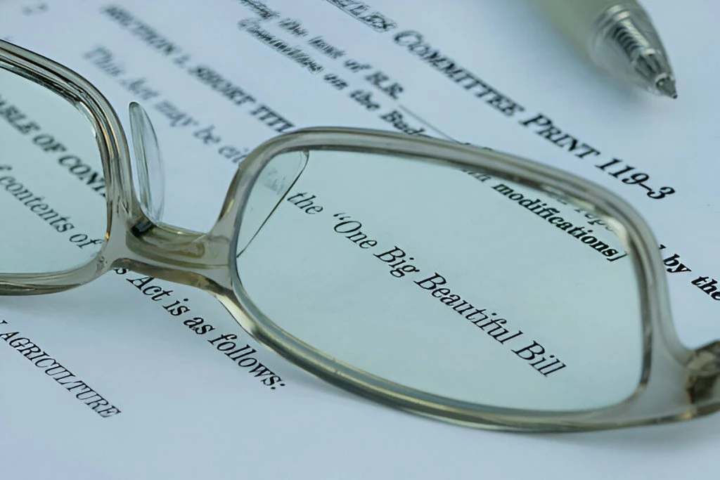 Eyeglasses and a pen rest on a printed document titled "One Big Beautiful Bill," highlighting the importance of reviewing the details within the "One Big Beautiful Bill" text, with other content partially visible underneath.