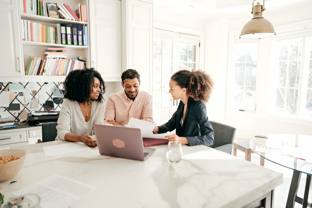 Three people sit at a kitchen table with a laptop and documents, engaging in a discussion about their One Big Beautiful Bill in a bright, modern room.